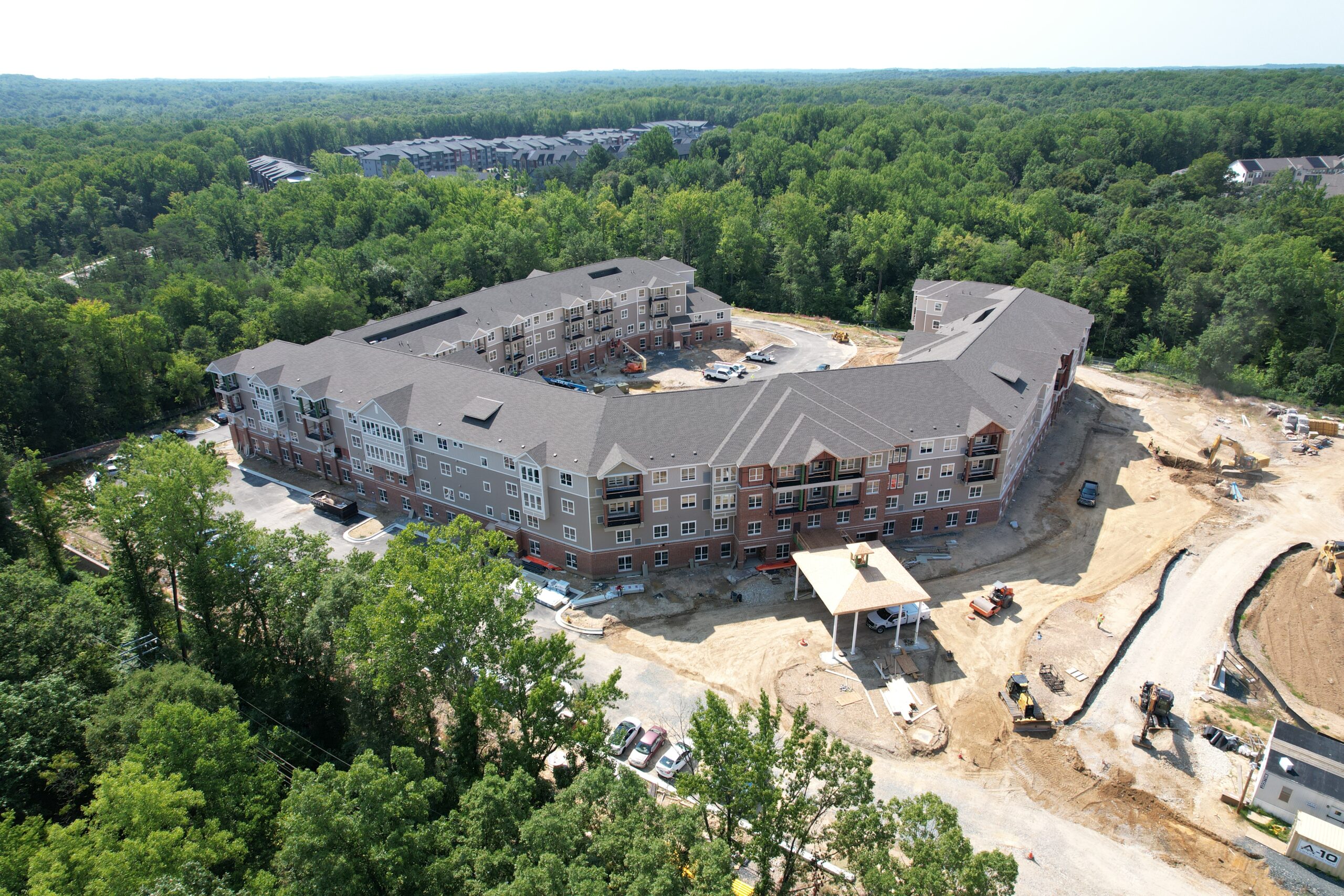 Aerial view of a U-shaped apartment complex under construction, surrounded by forest.