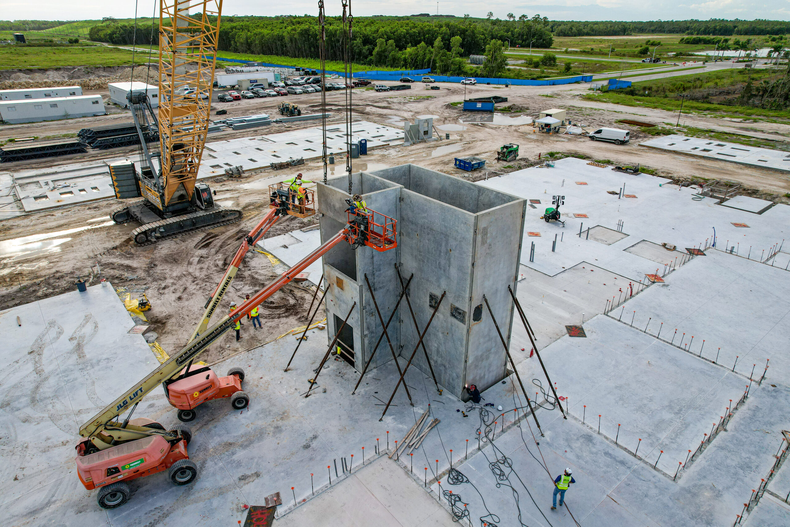 Aerial view of construction workers in a boom lift installing concrete panels on a building site.