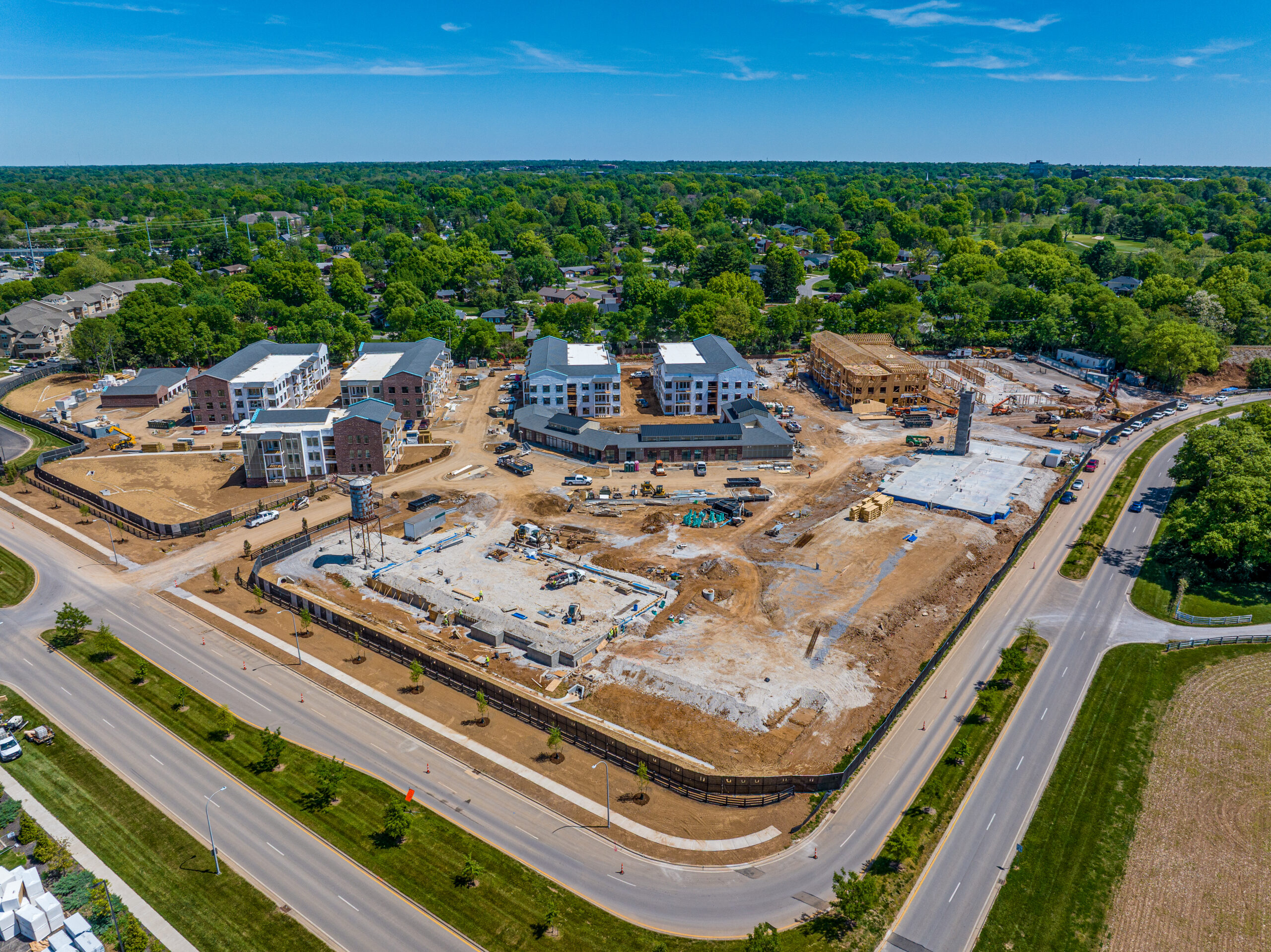 Aerial view of a residential construction site featuring several multi-story buildings in various stages of completion, surrounded by roads and wooded areas.