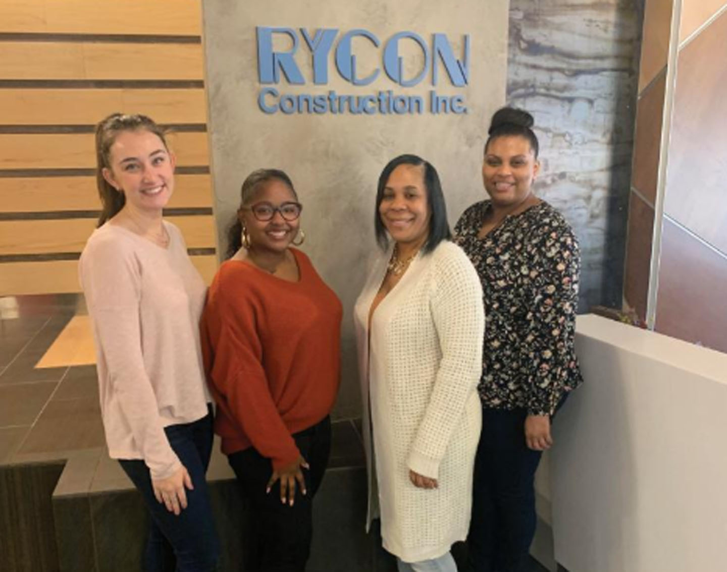 Four women standing in front of a Rycon Construction Inc. wall sign.
