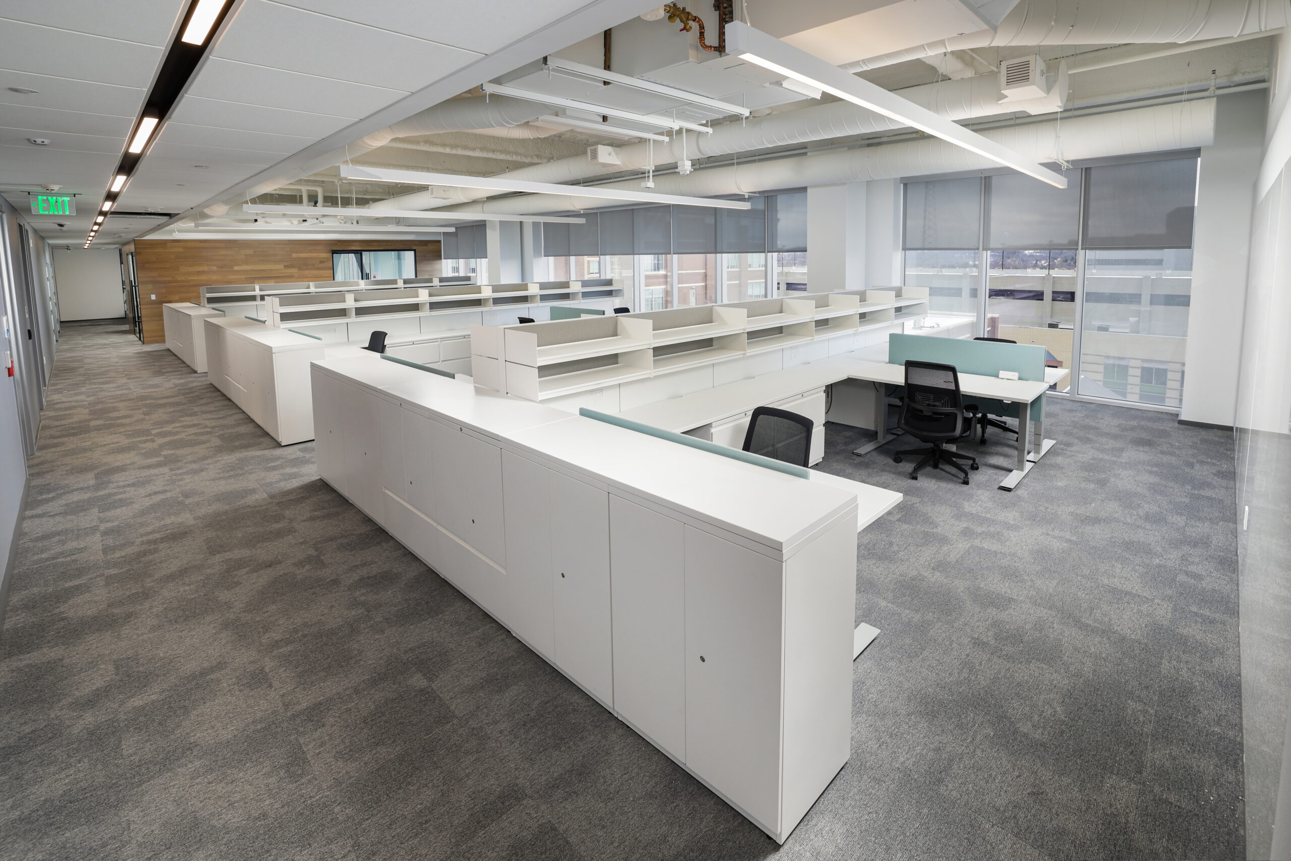 Glass-walled conference room featuring a long table with chairs, centered on a rug, with framed photos on the wall.