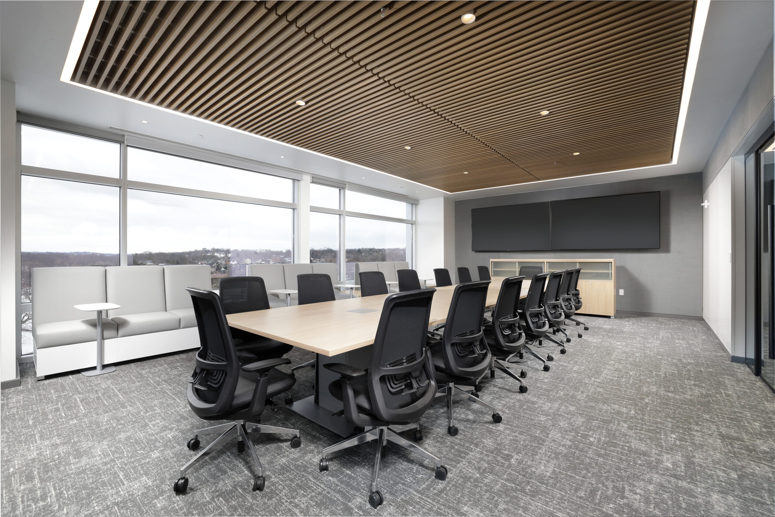 Modern conference room featuring a large wooden live-edge table surrounded by eight black office chairs on a light-colored rug.