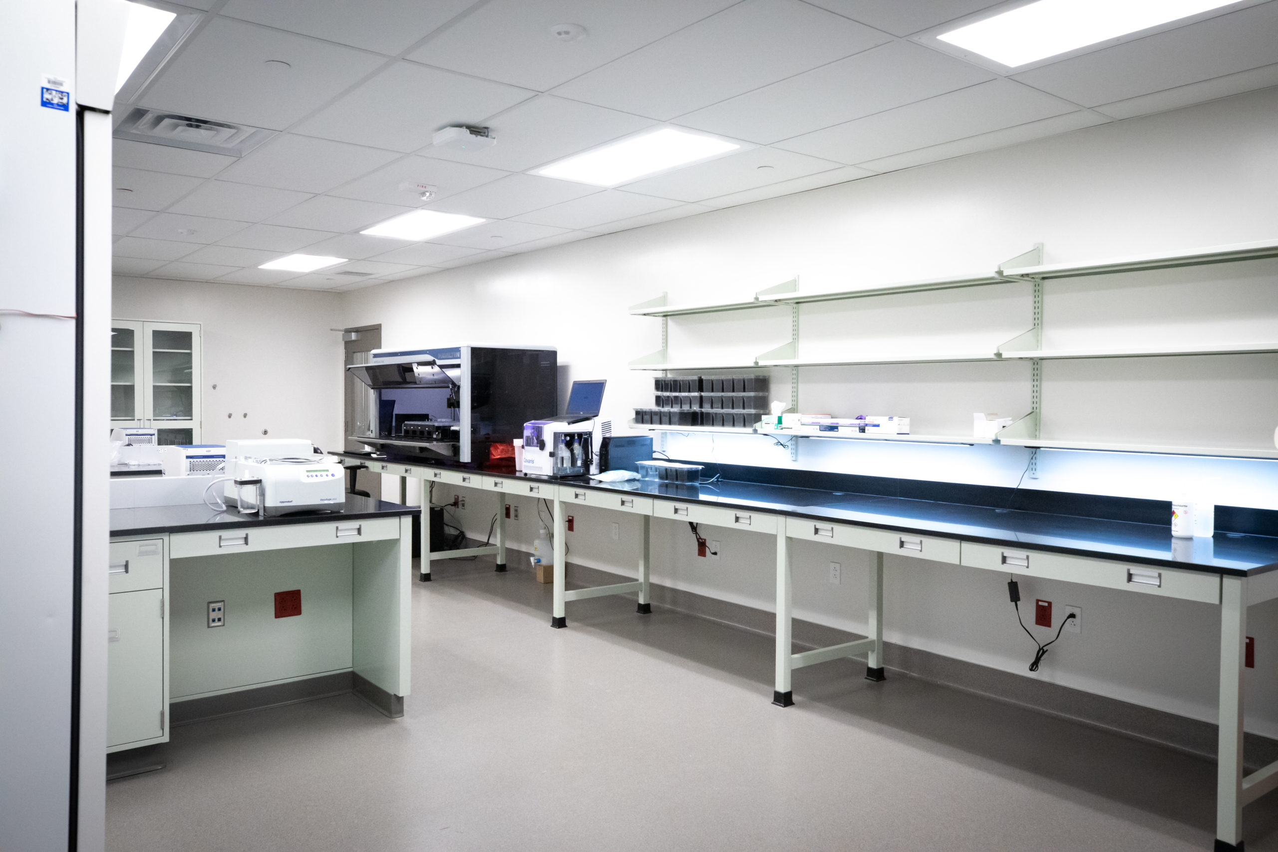 A laboratory with white walls, long black countertops, and equipment stations including a centrifuge and an automated analyzer.