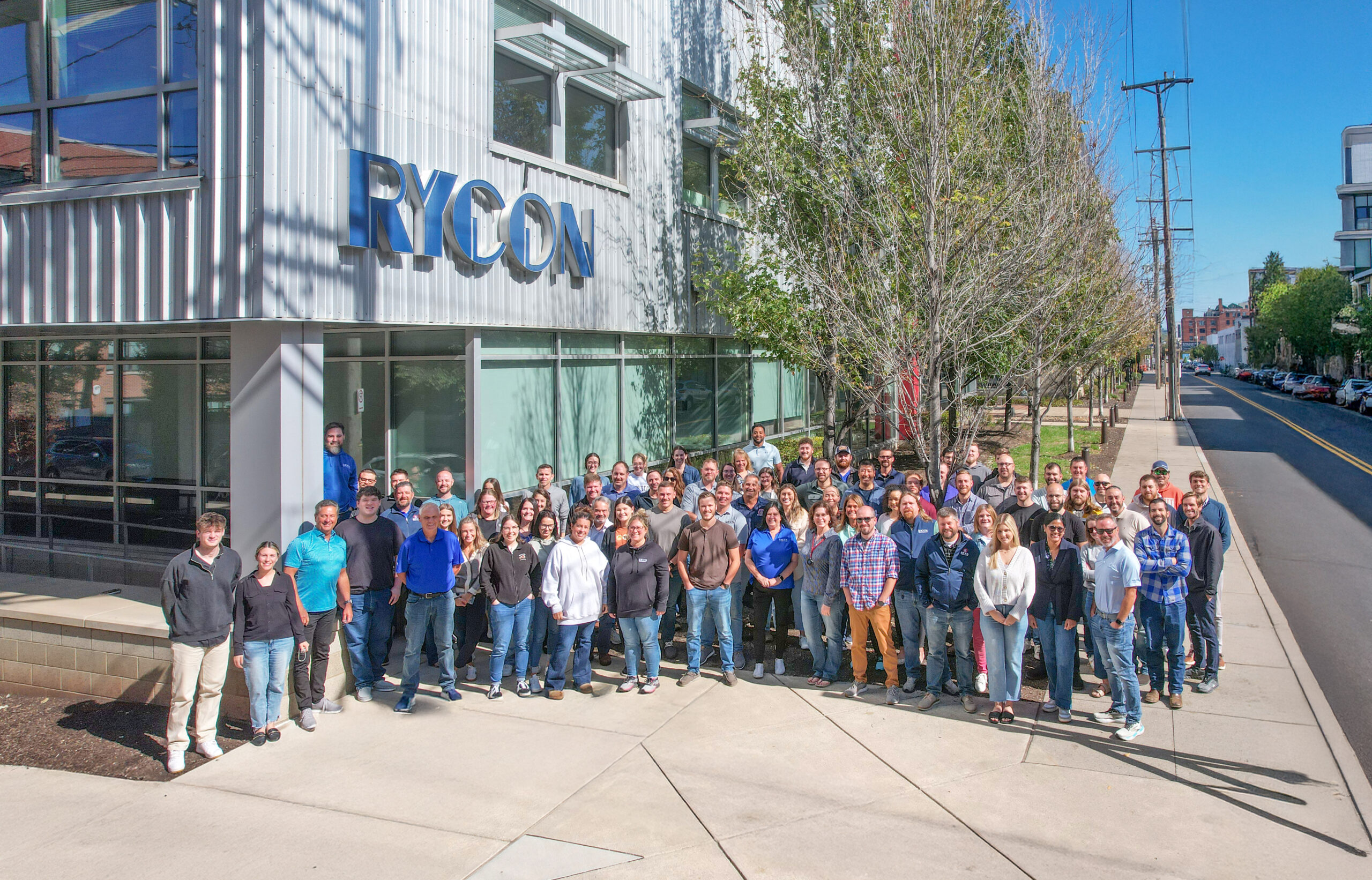 A large group of people posing for a photo in front of a Rycon office building.