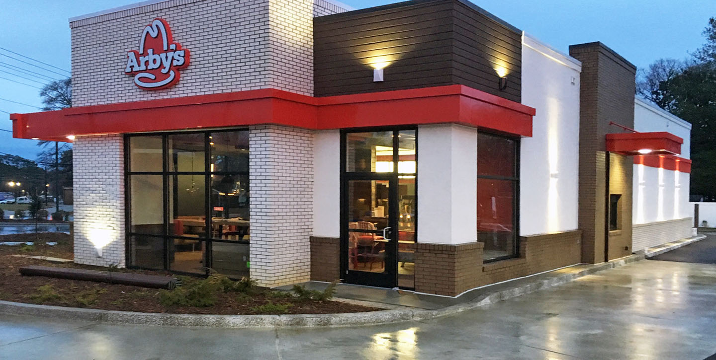 Exterior of an Arby’s restaurant featuring white brick and brown siding with the Arby’s logo above the entrance.