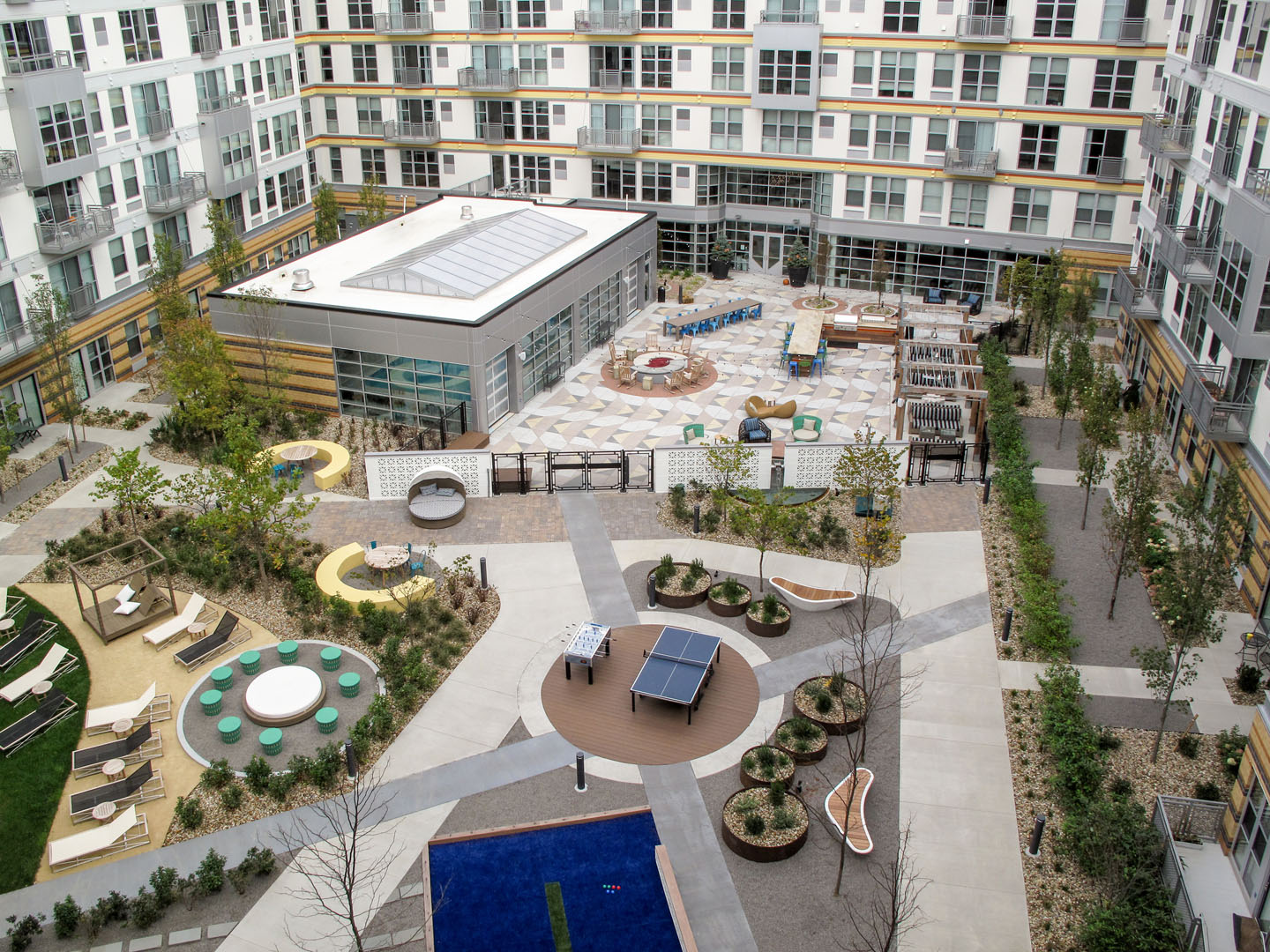 An elevated view of an apartment complex courtyard featuring walking paths, a ping pong table, lounge seating, and landscaped gardens.