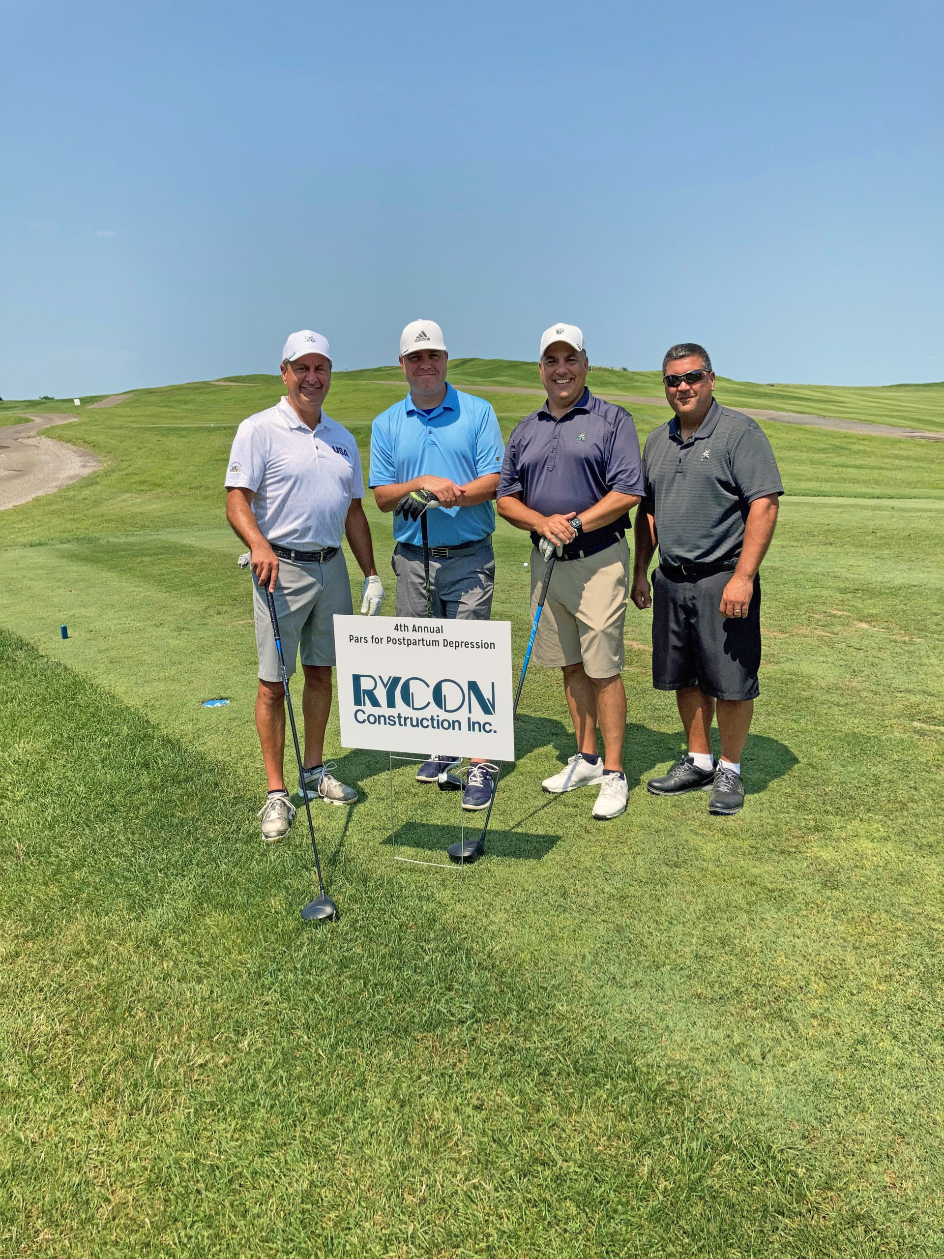 Four men in golf attire stand on a course behind a sign for the 4th Annual Pars for Postpartum Depression Rycon Construction Inc. golf tournament.