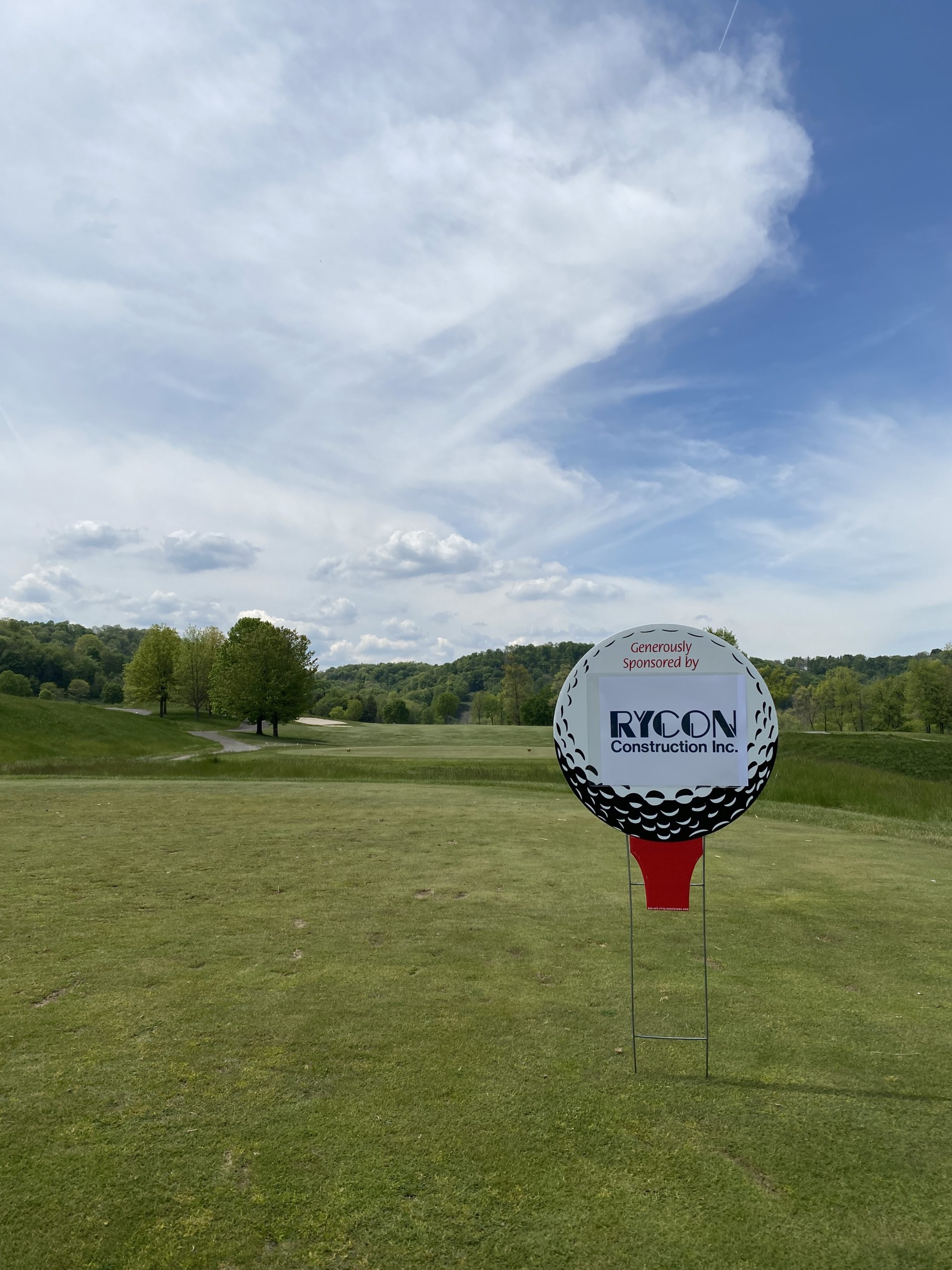 A golf course sponsor sign shaped like a golf ball on a tee, reading “Generously Sponsored by RYCON Construction Inc.”