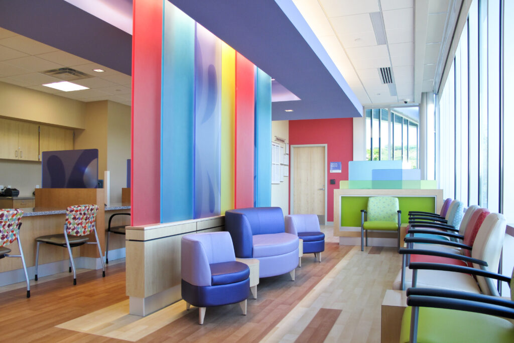 Modern medical waiting room featuring colorful modular seating and a floor-to-ceiling glass panel divider.