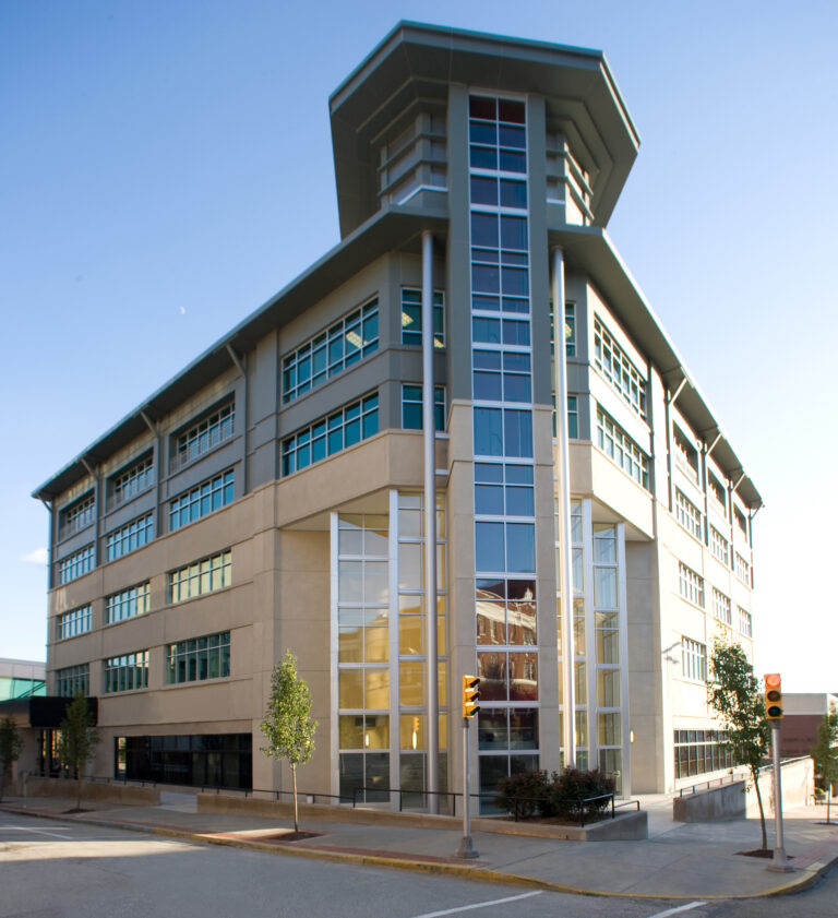 A multi-story office building with a corner tower, glass facade, and tan exterior panels.