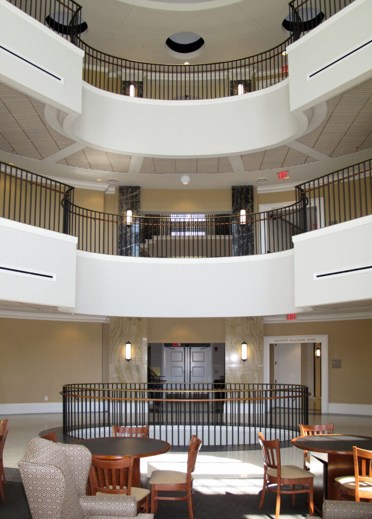 Multilevel circular atrium with tiered balconies, railings, and a ground-floor seating area with tables and chairs.