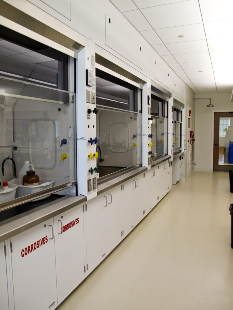 A row of laboratory fume hoods with cabinets labeled “CORROSIVES” below the counters.