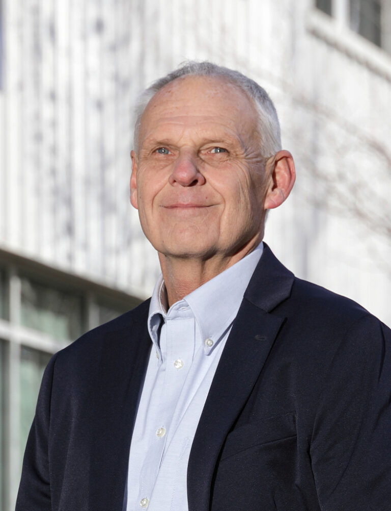 Headshot of a man with short gray hair wearing a dark blazer over a light button-down shirt.