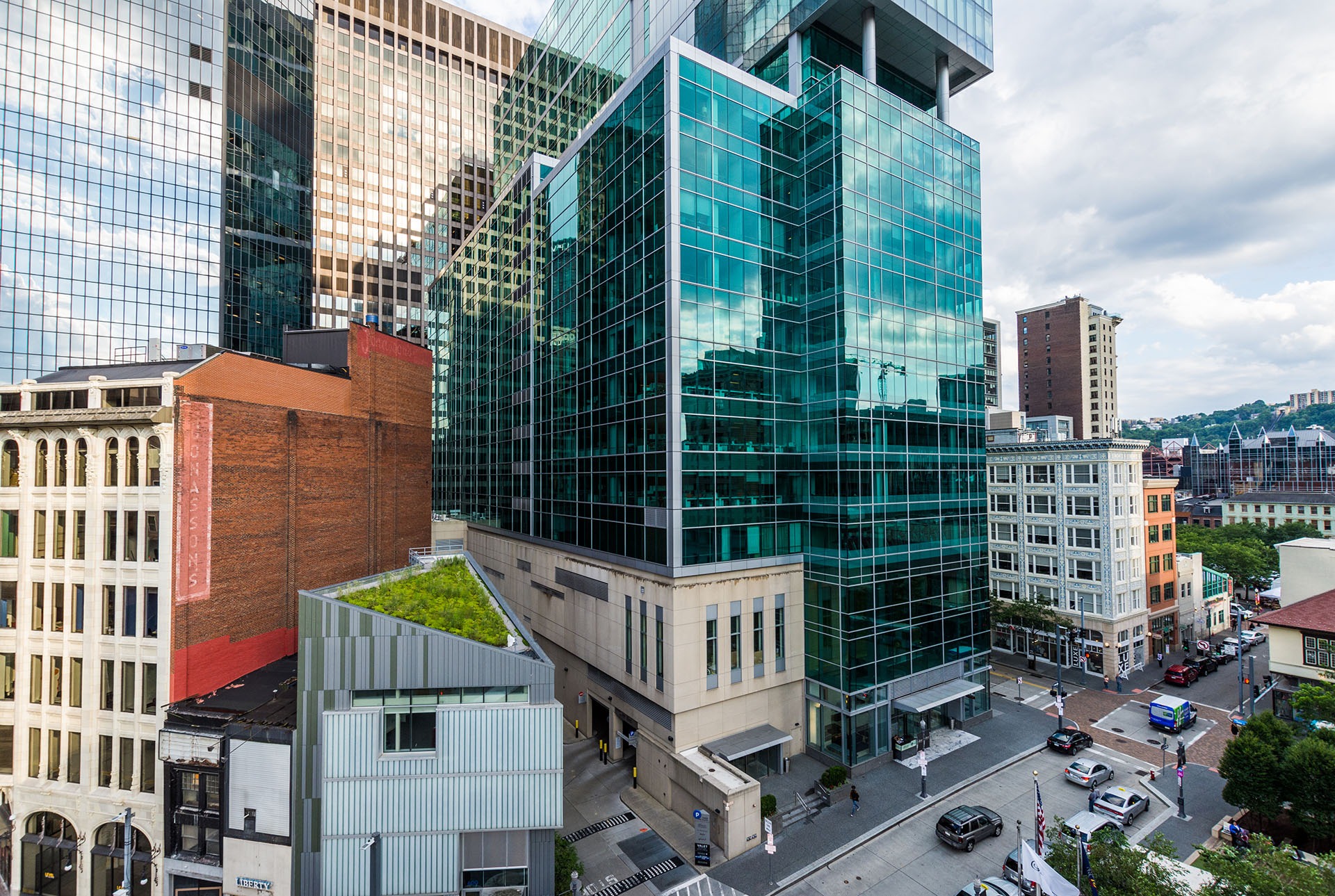 High-angle view of a city street featuring a large glass office tower, a smaller building with a green roof, and historic brick buildings.