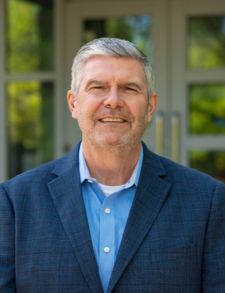 Headshot of a middle-aged man with gray hair wearing a blue button-down shirt and a navy blazer.