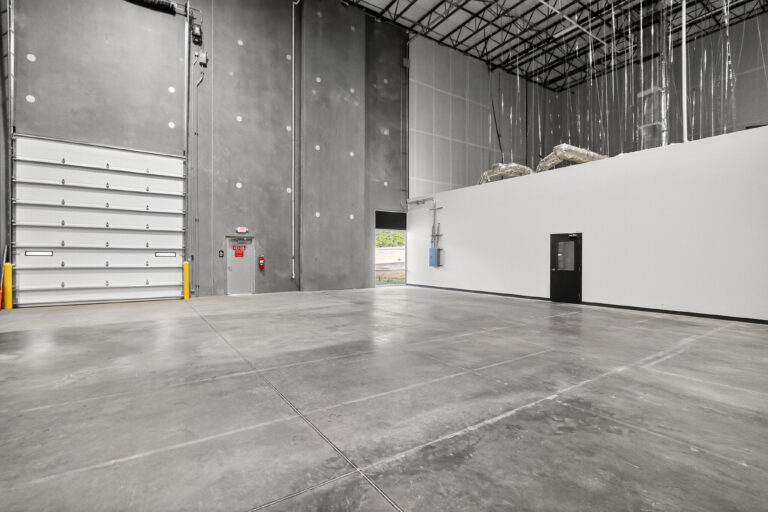A spacious industrial warehouse interior with concrete floors, a large roll-up door, and two entry doors.