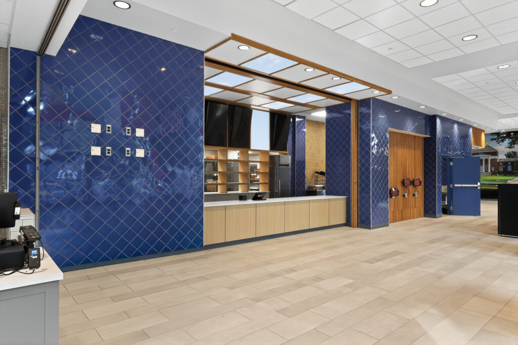 Empty service counter in a modern food court with blue tiled walls and wood paneling.