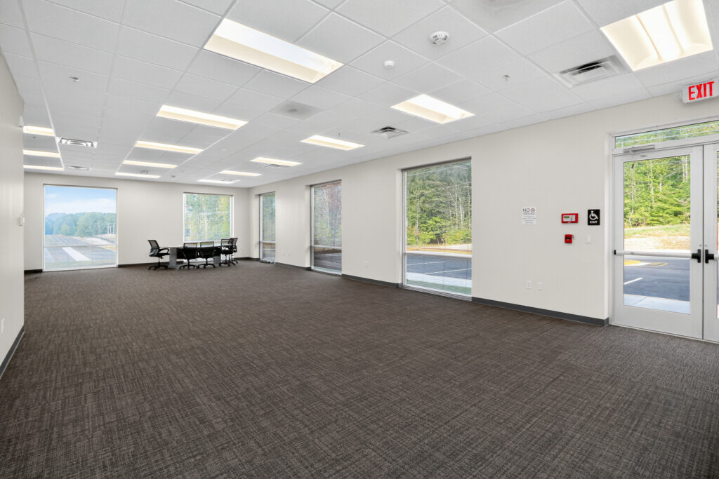 An empty, carpeted office space with large windows and a glass exit door.
