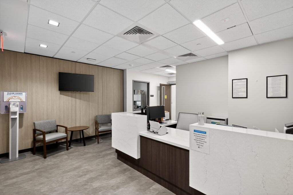 A medical reception area with a white marble-topped desk, a waiting area with two chairs, and informational signs on the walls.