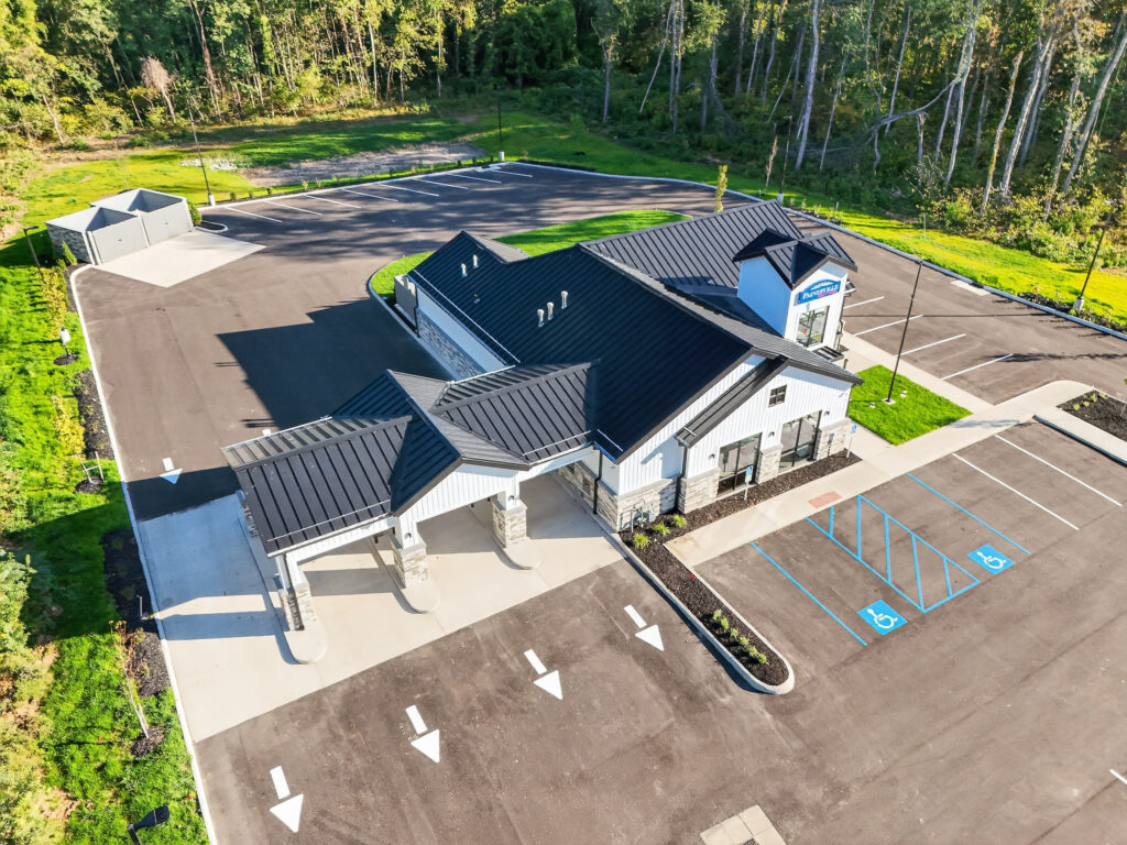 Aerial view of a commercial building with a black metal roof, a drive-thru lane, and a parking lot with designated accessible spaces.