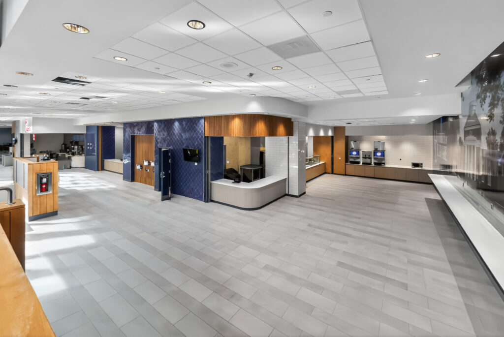 Modern office breakroom or cafeteria area with a service counter, beverage machines, and tiled flooring.