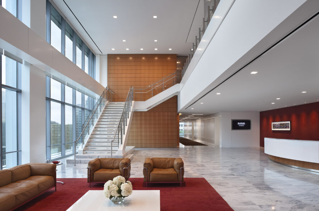 Spacious modern office lobby with a central staircase, leather seating, and a reception desk.