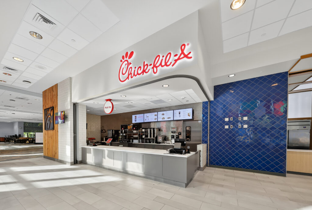 A Chick-fil-A restaurant counter featuring a digital menu board and a red “Pick Up” sign.