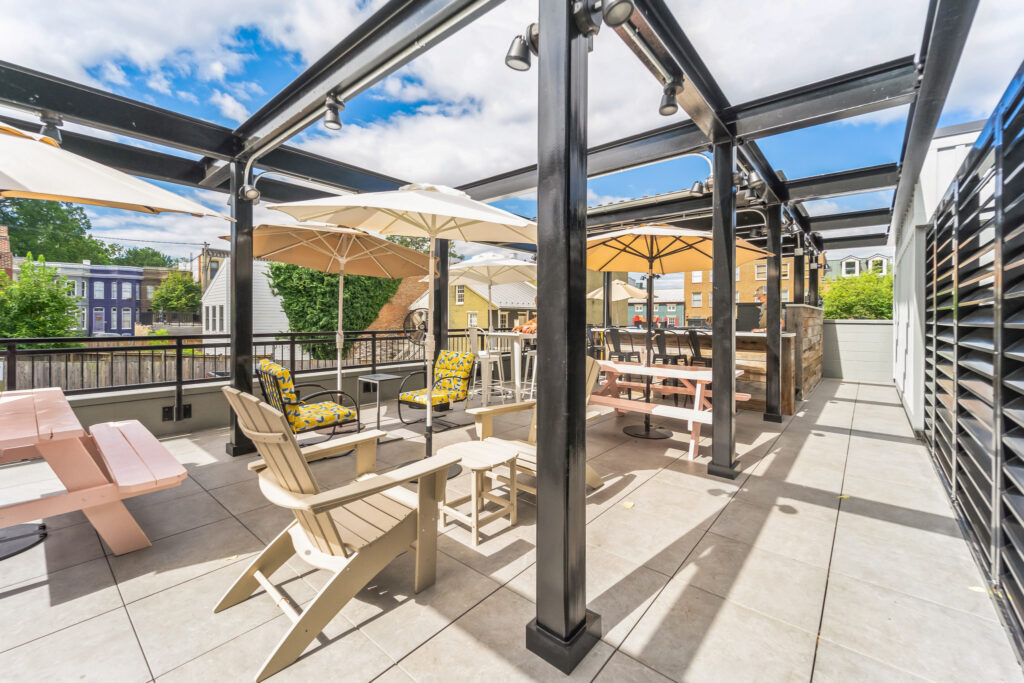 Rooftop patio with shaded outdoor seating, including Adirondack chairs, a picnic table, and a bar area under a metal pergola.