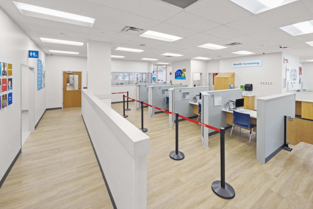 A plasma donation center interior with a health screening area, partitioned workstations, and a queue line.