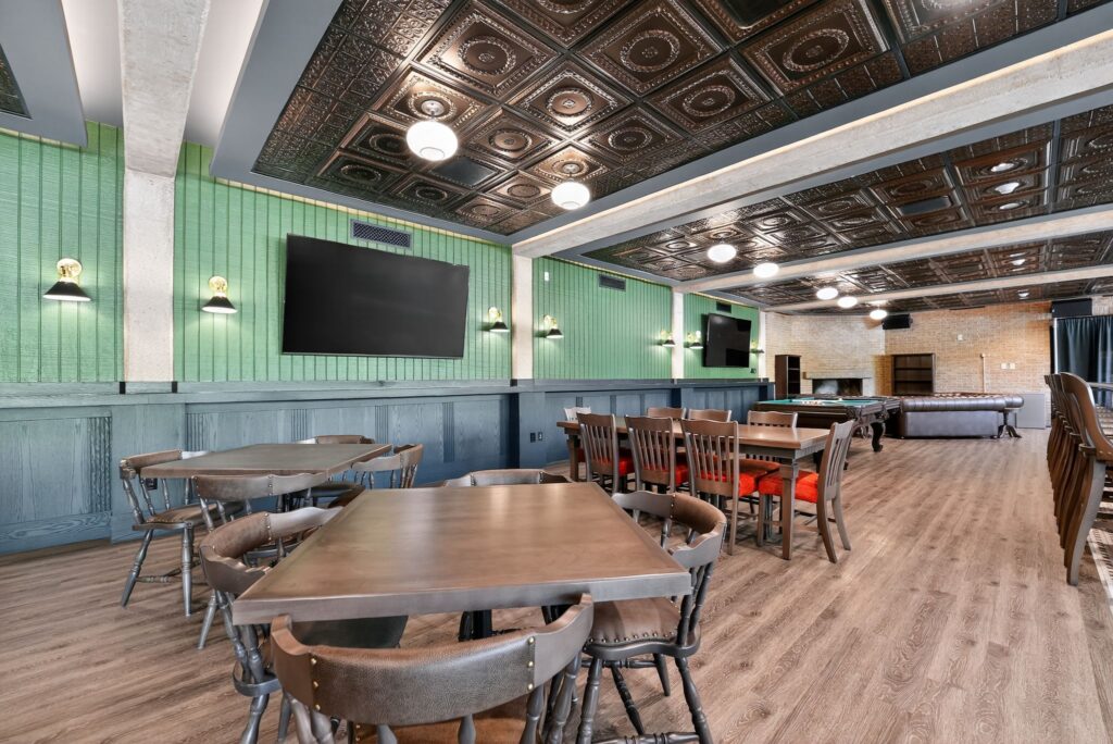Restaurant interior with dark wood tables, spindle-back chairs, green paneled walls, and a decorative metallic ceiling.