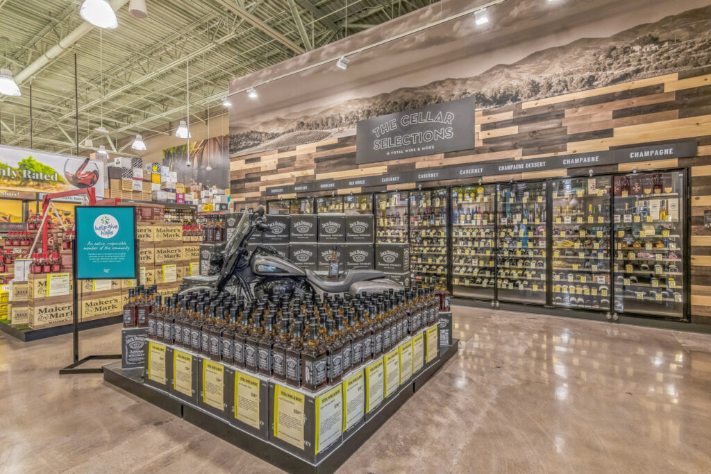 A retail liquor store display featuring a decorative motorcycle surrounded by rows of Jack Daniel’s whiskey bottles, positioned in front of refrigerated wine coolers.