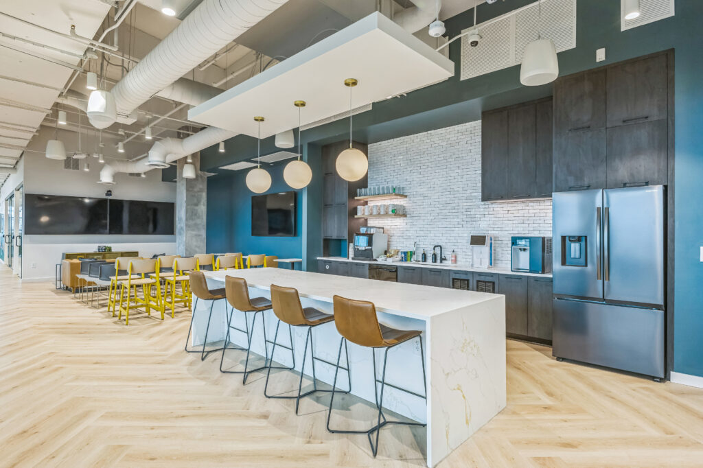 Office break room featuring a marble-topped island with four stools, dark cabinetry, stainless steel appliances, and a tiled backsplash.