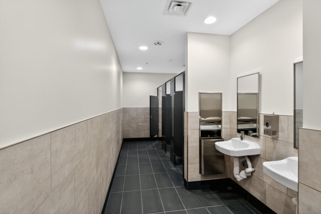 Public restroom with two wall-mounted sinks, a paper towel dispenser, and a row of bathroom stalls.