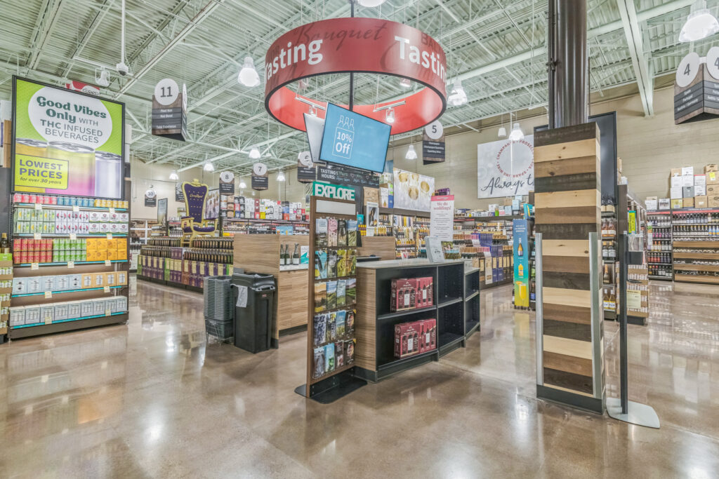Interior of a liquor store with numbered aisle signs, a central tasting area, and signage advertising THC-infused beverages.