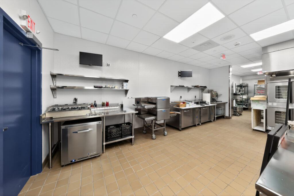 A commercial kitchen with stainless steel countertops, equipment, and shelves against a white wall.