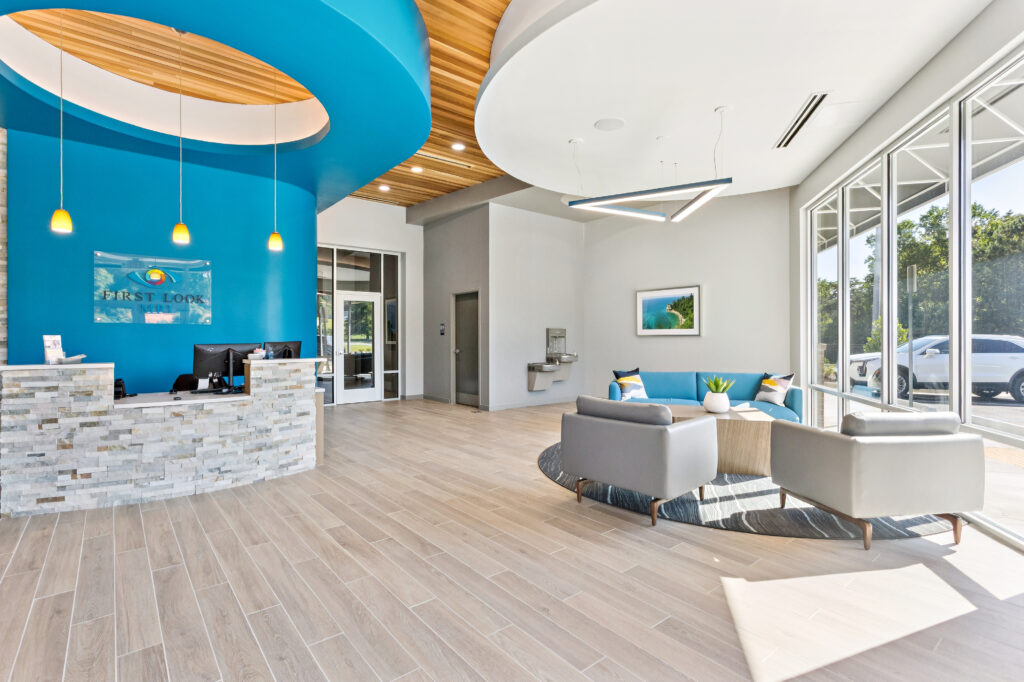 Reception area with a blue desk, wood-slatted ceiling, and a seating area featuring a blue sofa and two grey armchairs.