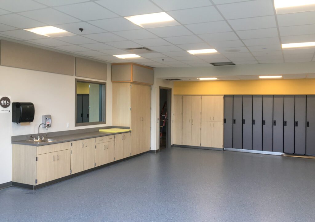 A room featuring a sink, counter space, wooden cabinets, and a row of grey lockers.
