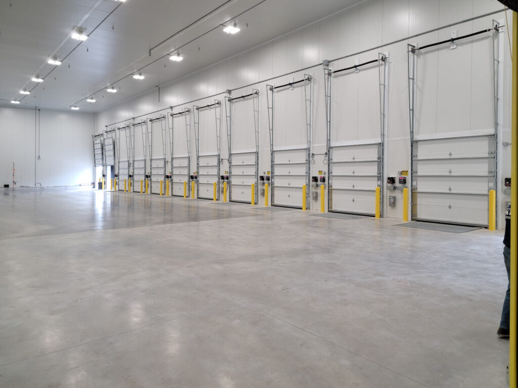 A row of closed loading dock doors in a large, empty warehouse.