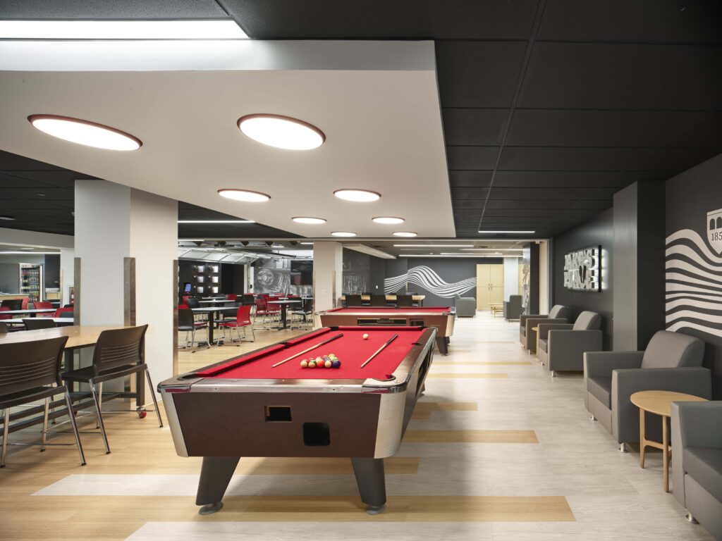 A recreation room with two pool tables, seating areas with armchairs, and dining tables.