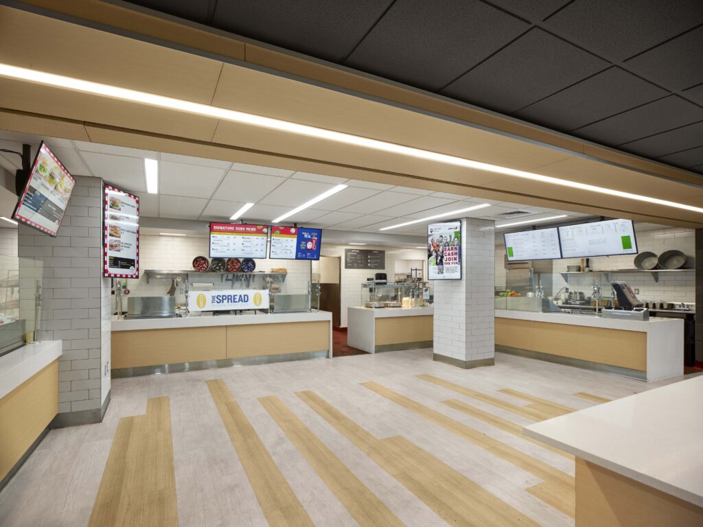 An empty cafeteria serving line with digital menu boards and a sign that reads “The Spread.”