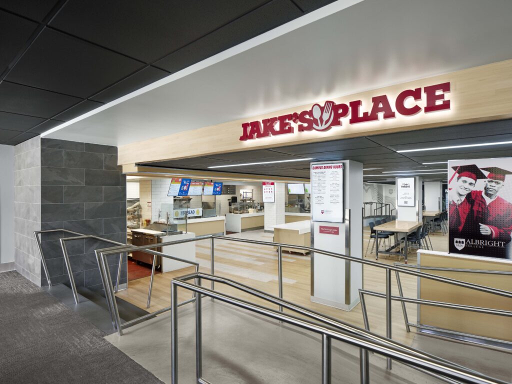 Entrance to Jake’s Place dining hall with metal railings in the foreground and a menu board visible inside.
