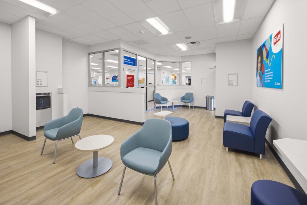 Waiting room with blue armchairs, small tables, and a donation center sign on the wall.