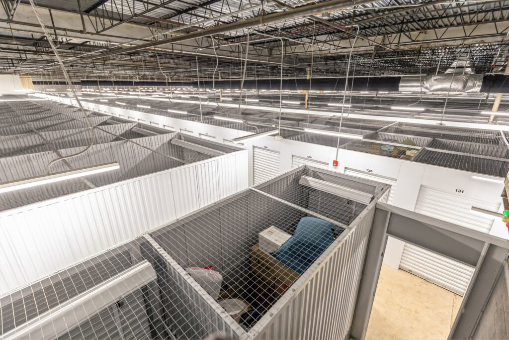 High-angle view of a large indoor self-storage facility featuring multiple rows of metal units with wire mesh ceilings.