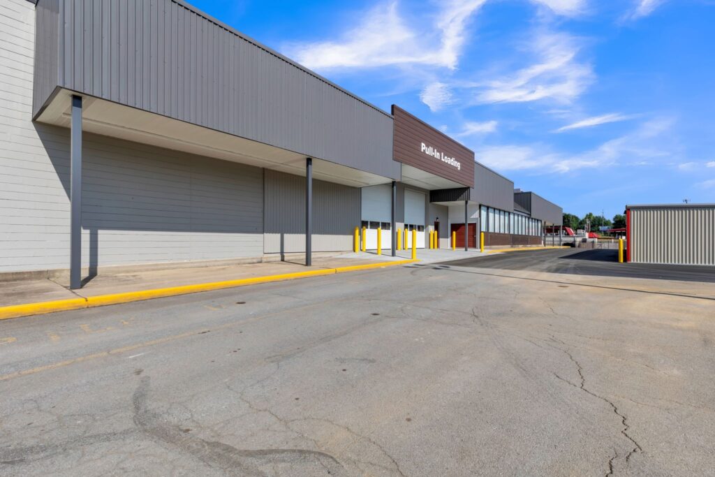 Commercial building exterior featuring a pull-in loading bay with white garage doors and a yellow-painted curb.