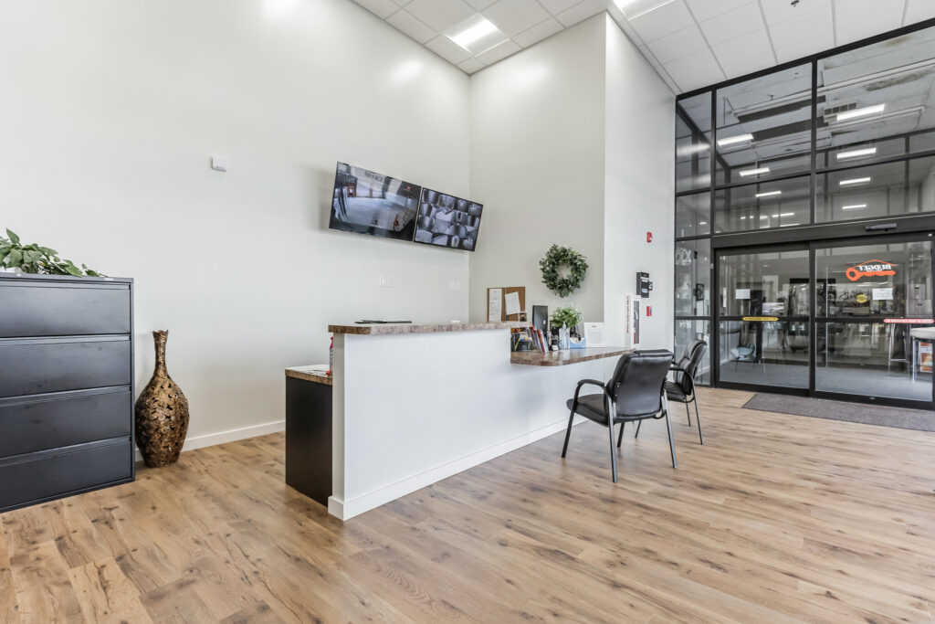 Reception desk in a bright office lobby with wood flooring, a tall black filing cabinet, and glass double doors leading to the exterior.