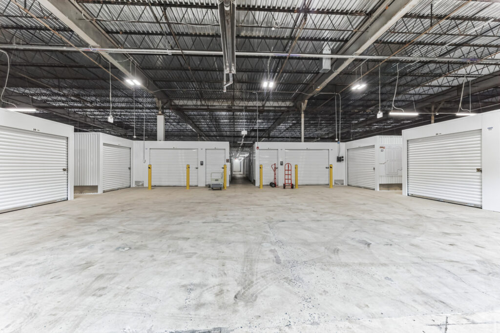 Indoor storage facility hallway with rows of white roll-up unit doors and a concrete floor.
