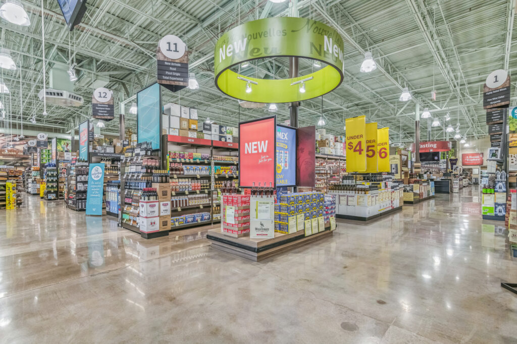 Interior view of a liquor store featuring aisles, displays of wine and spirits, and overhead signage for sections and promotions.