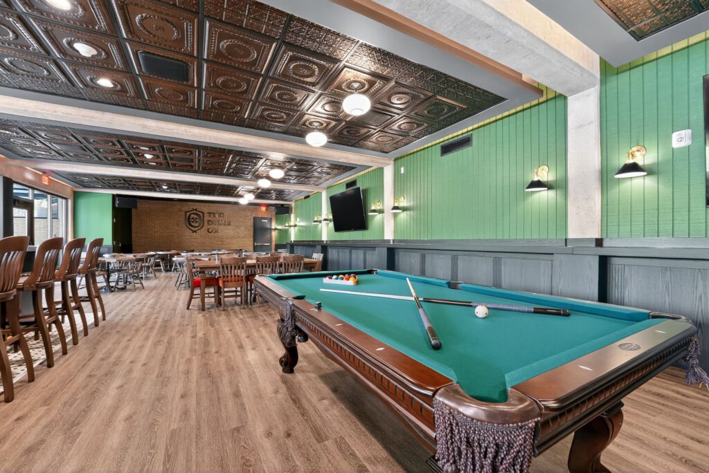 A billiards table in a dining room with a green paneled wall and a patterned metal ceiling.