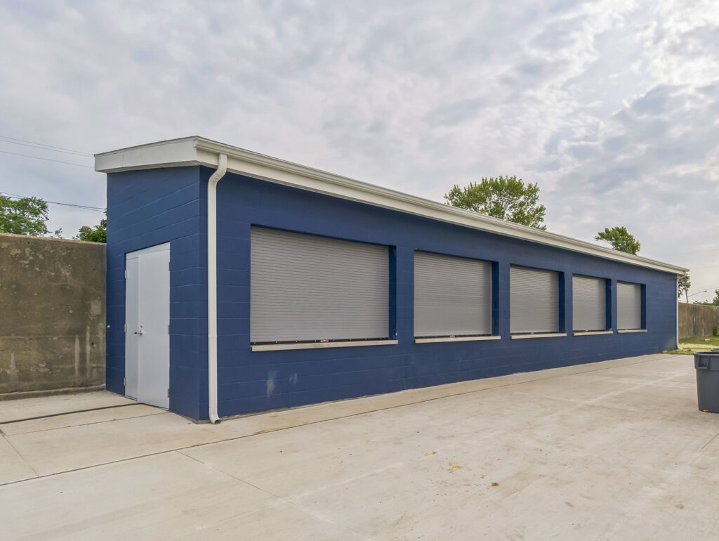 Blue single-story building with a white door and five closed metal shutters.