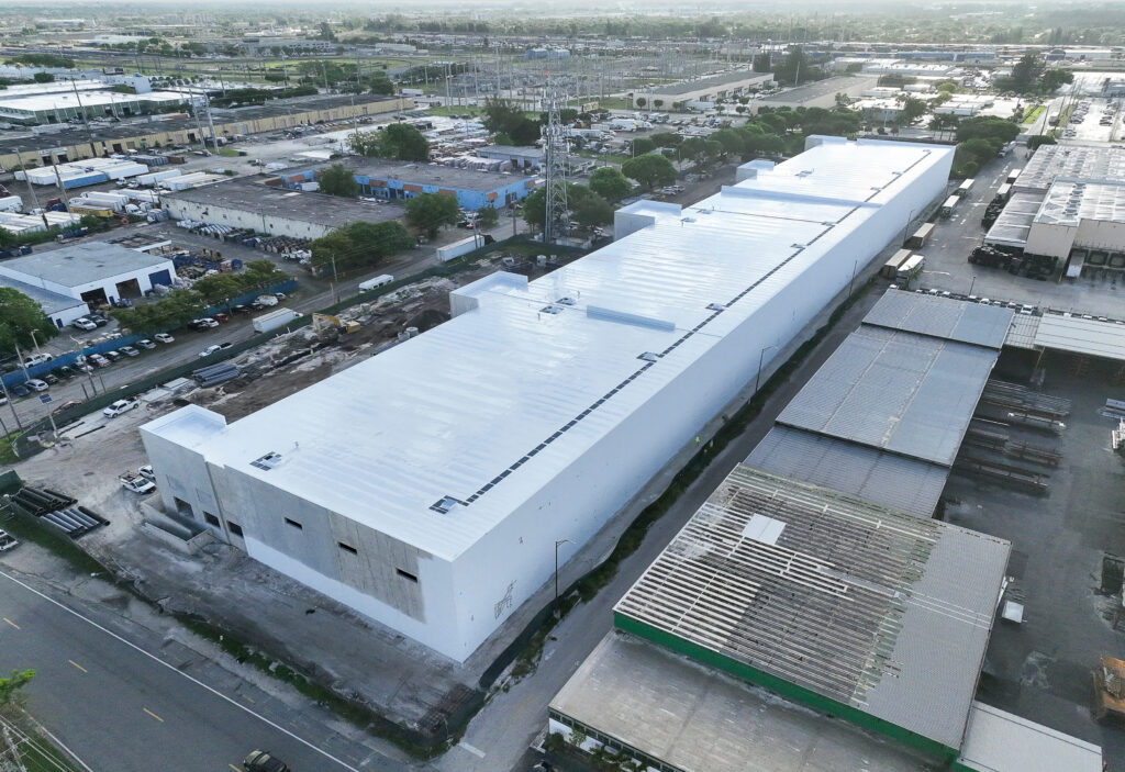 Aerial view of a long, white industrial building under construction in a commercial area.